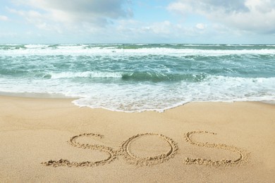 Message SOS drawn on sand near wavy sea