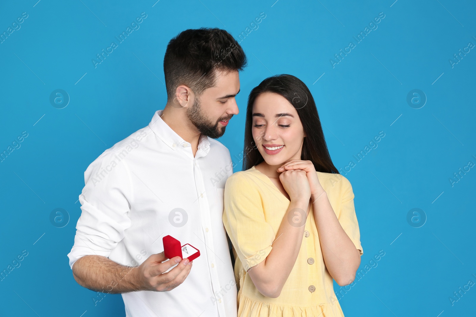 Photo of Man with engagement ring making marriage proposal to girlfriend on blue background