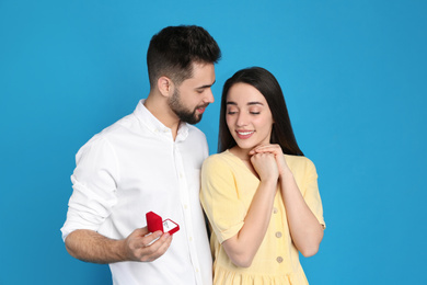 Man with engagement ring making marriage proposal to girlfriend on blue background