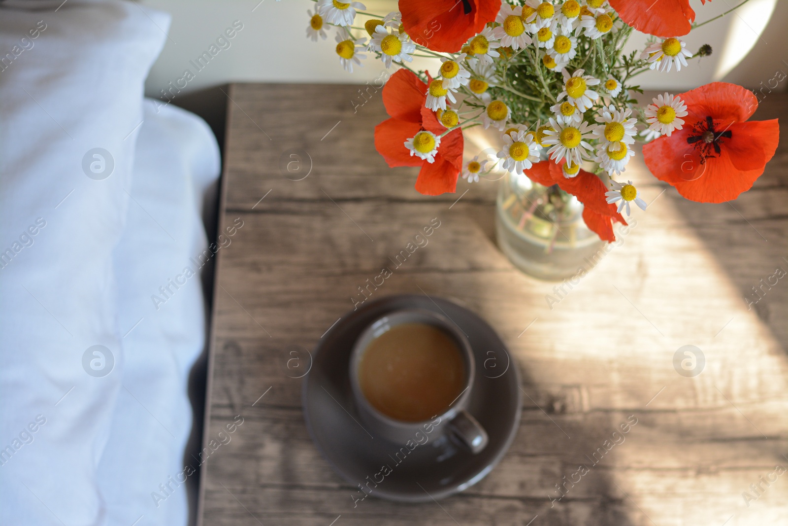 Photo of Beautiful bouquet of poppies and chamomiles near cup with coffee indoors, focus on flowers