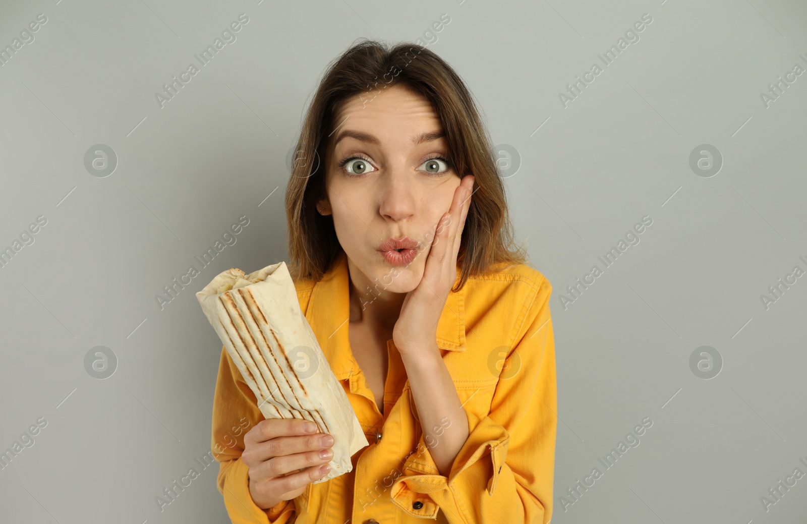 Photo of Emotional young woman with delicious shawarma on grey background