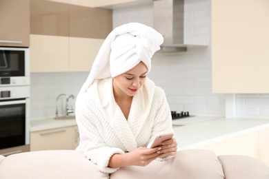 Photo of Beautiful woman with hair wrapped in towel using smartphone at home