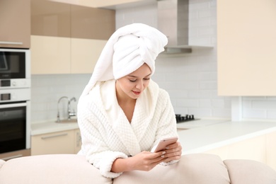 Beautiful woman with hair wrapped in towel using smartphone at home