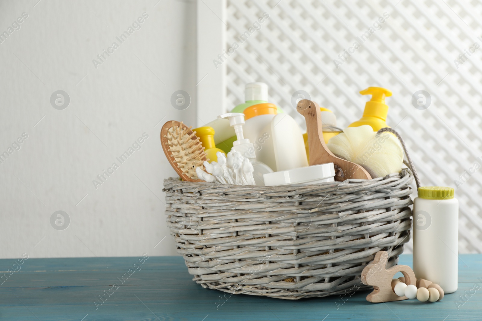 Photo of Wicker basket with different baby cosmetic products, accessories and toys on light blue wooden table. Space for text