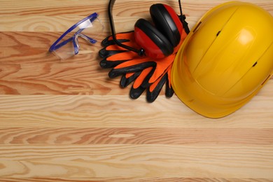 Photo of Hard hat, earmuffs, gloves and goggles on wooden table, flat lay with space for text. Safety equipment