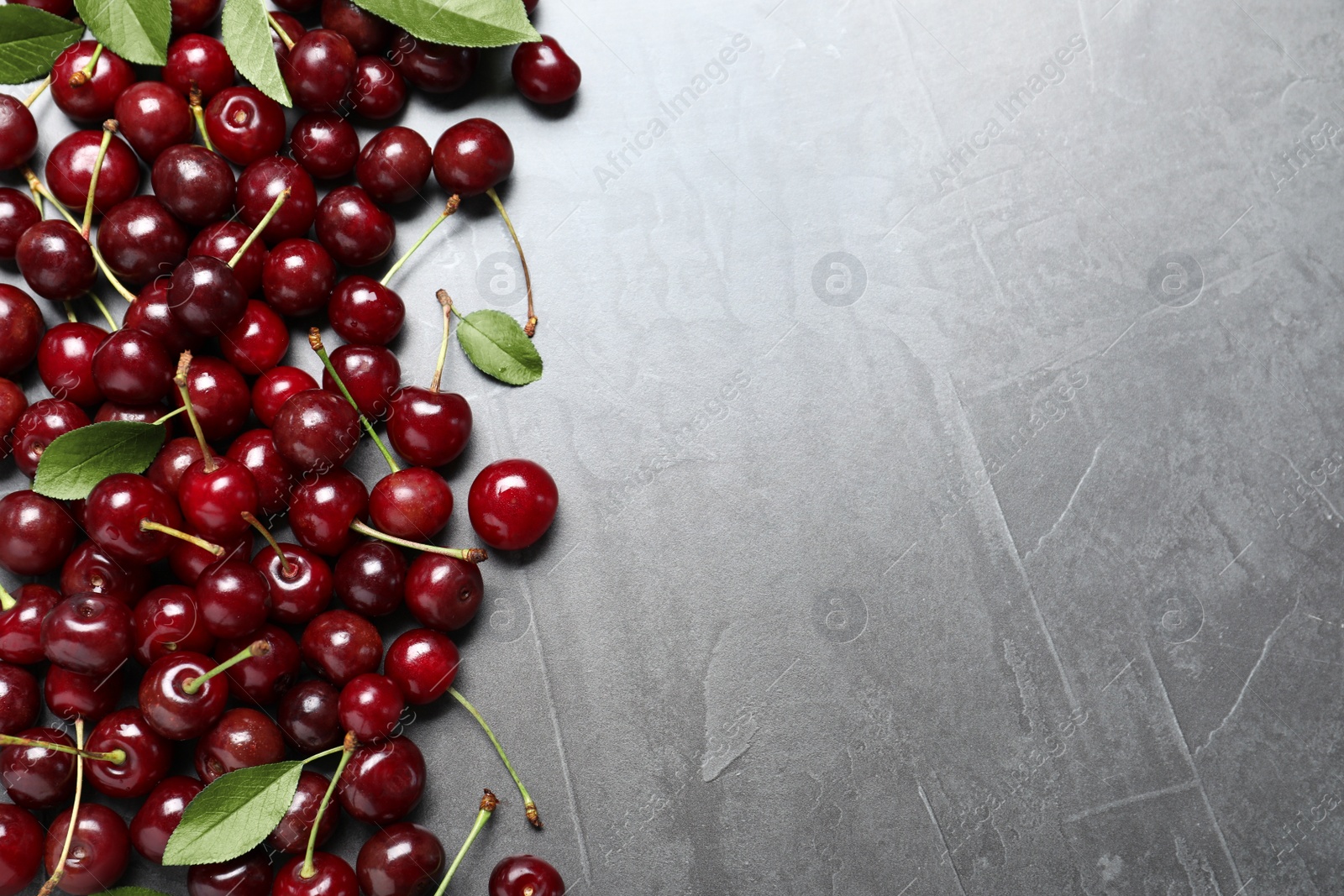 Photo of Sweet juicy cherries with leaves on grey table, flat lay. Space for text