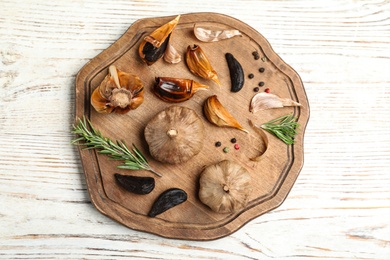 Board with black garlic and rosemary on white wooden table, top view