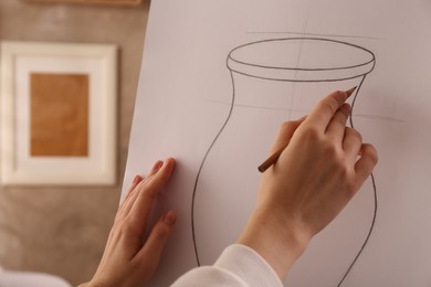 Photo of Woman drawing vase with graphite pencil on canvas indoors, closeup
