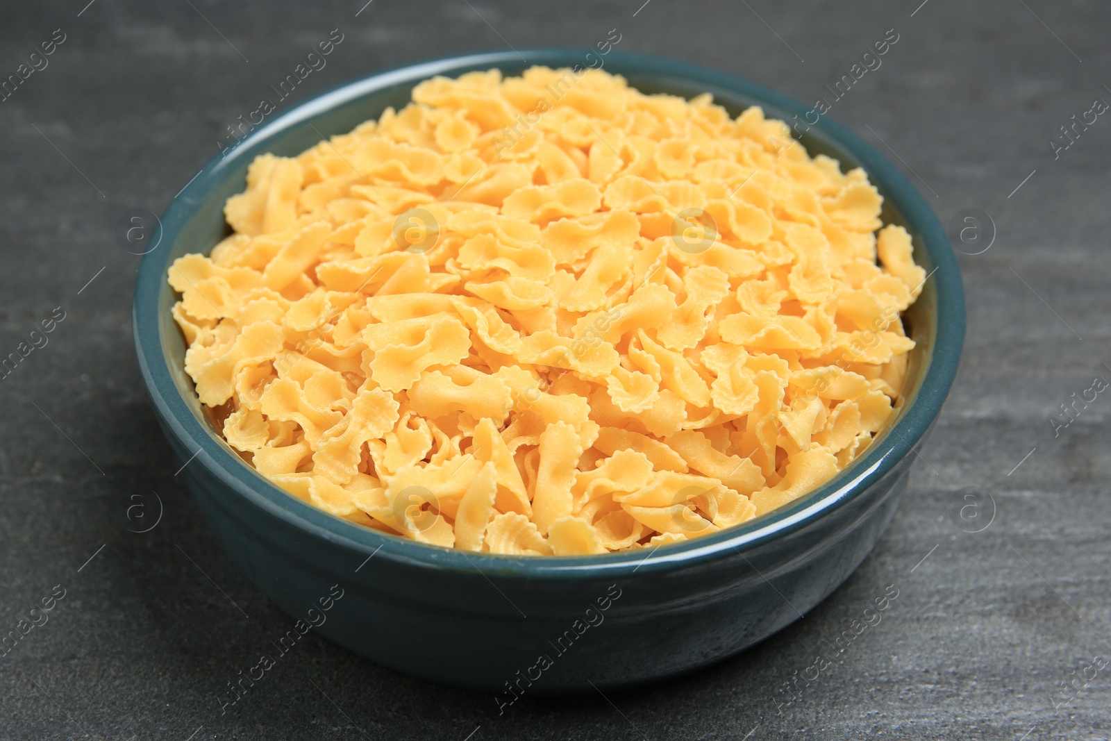 Photo of Raw farfalline pasta in bowl on grey table, closeup
