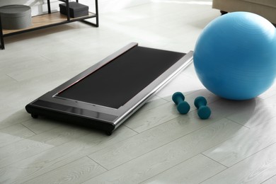 Photo of Modern walking treadmill, dumbbells and fitness ball in living room. Home gym equipment