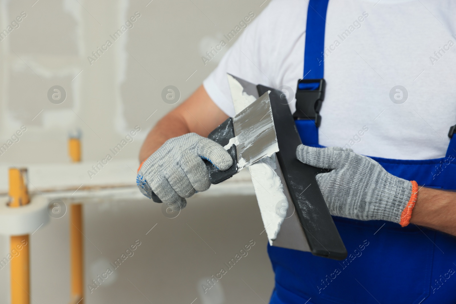 Photo of Worker with putty knives and plaster near wall, closeup