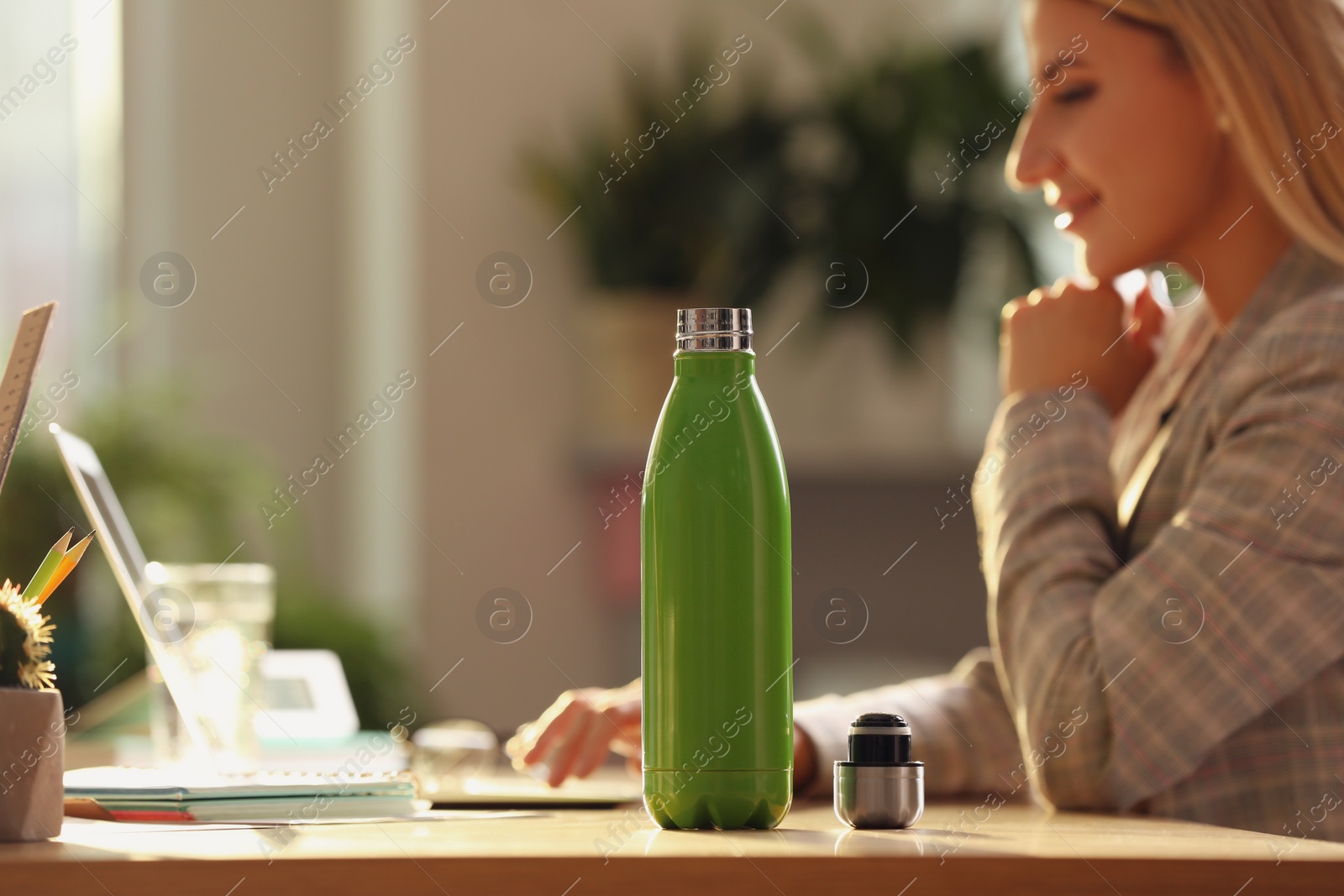 Photo of Woman working at table in modern office, focus on green thermos bottle