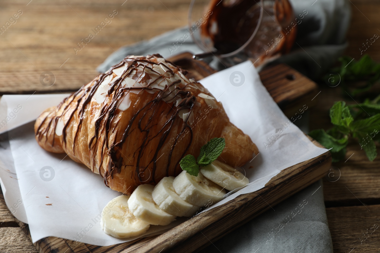 Photo of Delicious croissant with chocolate and banana on wooden table, closeup