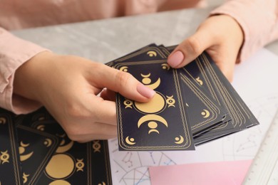 Woman using tarot cards at table, closeup. Astrological predictions