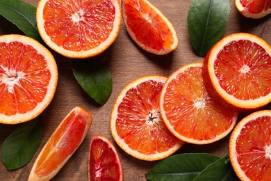 Photo of Slices of fresh ripe red oranges and green leaves on wooden table, flat lay