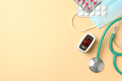 Photo of Flat lay composition with fingertip pulse oximeter and medical items on light orange background. Space for text