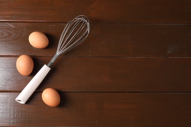 Photo of Metal whisk and raw eggs on wooden table, flat lay. Space for text
