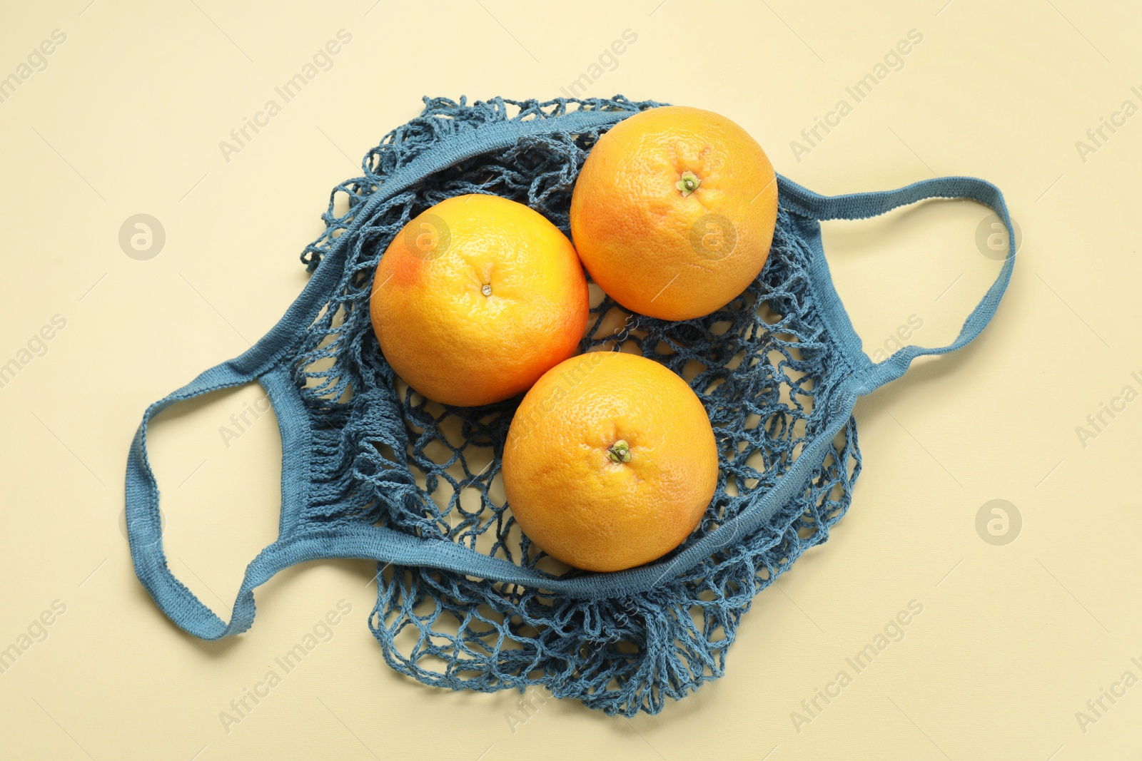 Photo of String bag with oranges on beige background, top view