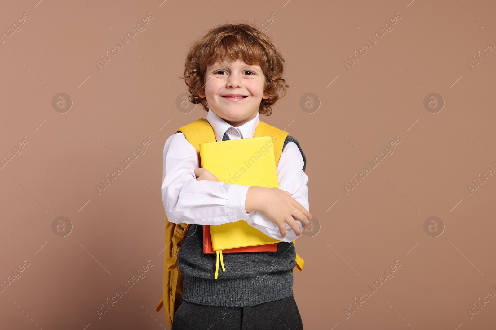 Photo of Happy schoolboy with backpack and books on brown background