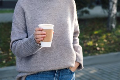 Photo of Woman holding takeaway cardboard cup on city street, closeup. Coffee to go