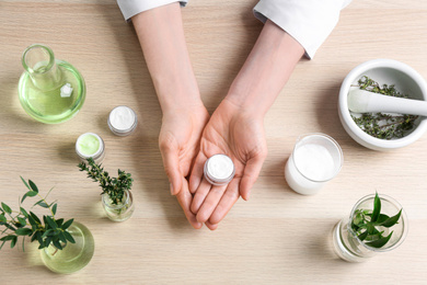 Photo of Woman with natural cream at wooden table in cosmetic laboratory, top view