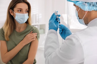 Doctor filling syringe with vaccine against Covid-19 while patient waiting for injection in clinic