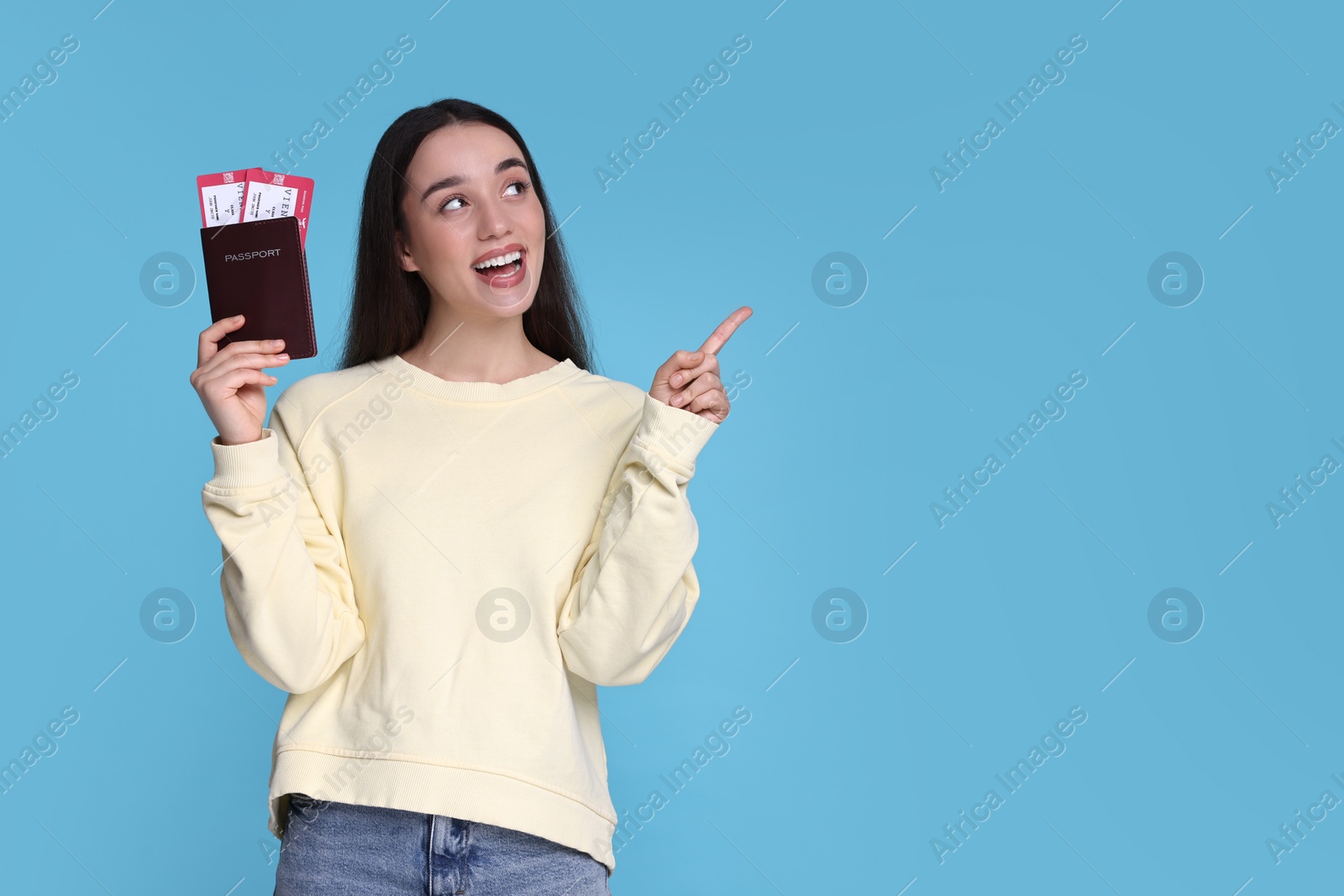 Photo of Happy woman with passport and tickets pointing at something on light blue background. Space for text