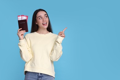 Happy woman with passport and tickets pointing at something on light blue background. Space for text