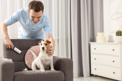 Photo of Smiling man removing pet's hair from armchair at home. Space for text