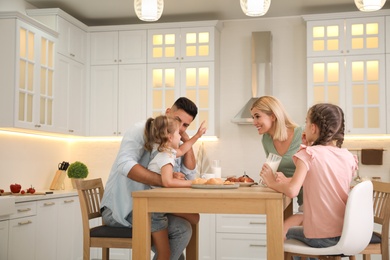 Photo of Happy family eating together at table in modern kitchen