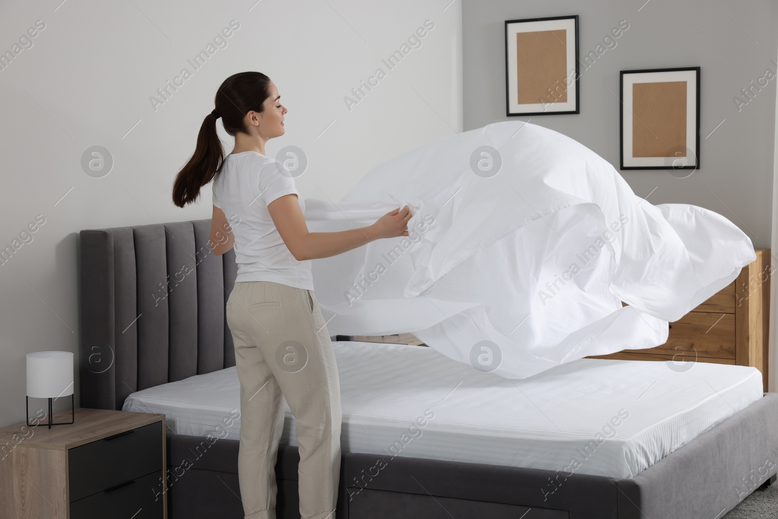 Photo of Young woman changing bed linens at home