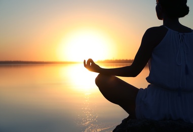 Photo of Woman practicing yoga near river on sunset, closeup. Healing concept