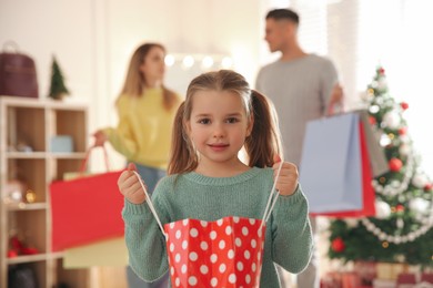 Photo of Little girl with bag near her parents in store. Family Christmas shopping