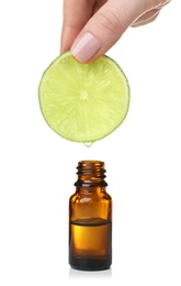 Photo of Woman holding slice of lime above bottle with essential oil on white background