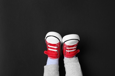 Little child in stylish red gumshoes on black background, top view