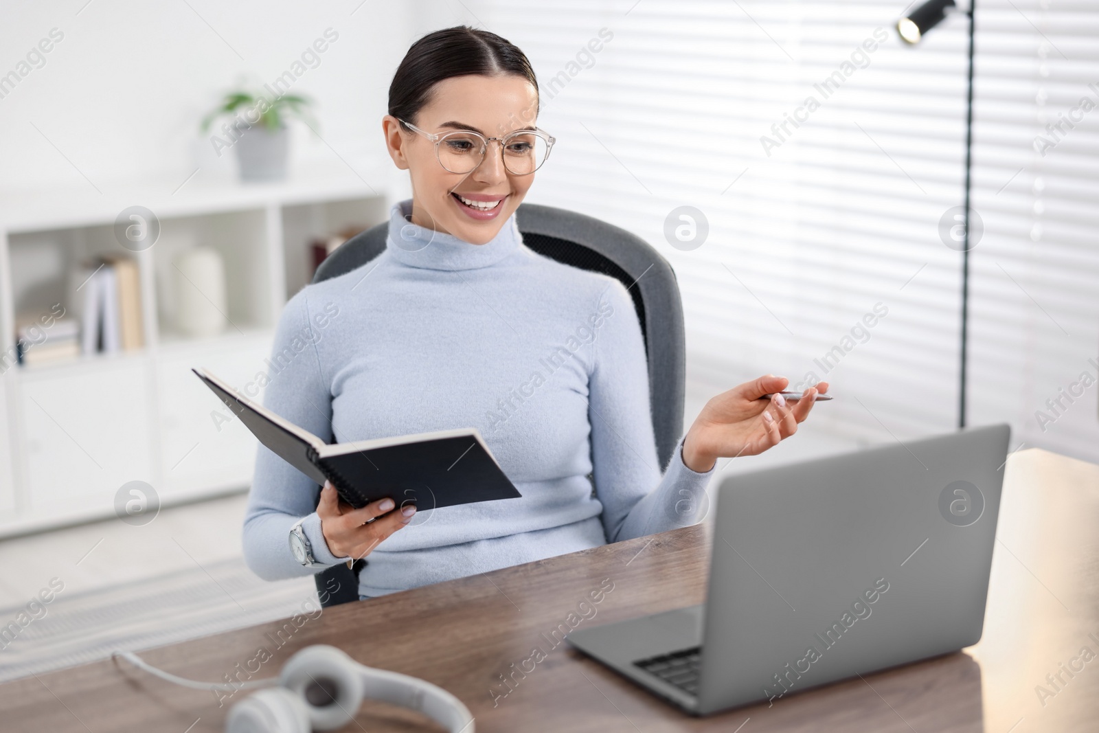 Photo of Young woman in glasses using video chat during webinar at table in office