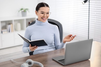 Young woman in glasses using video chat during webinar at table in office