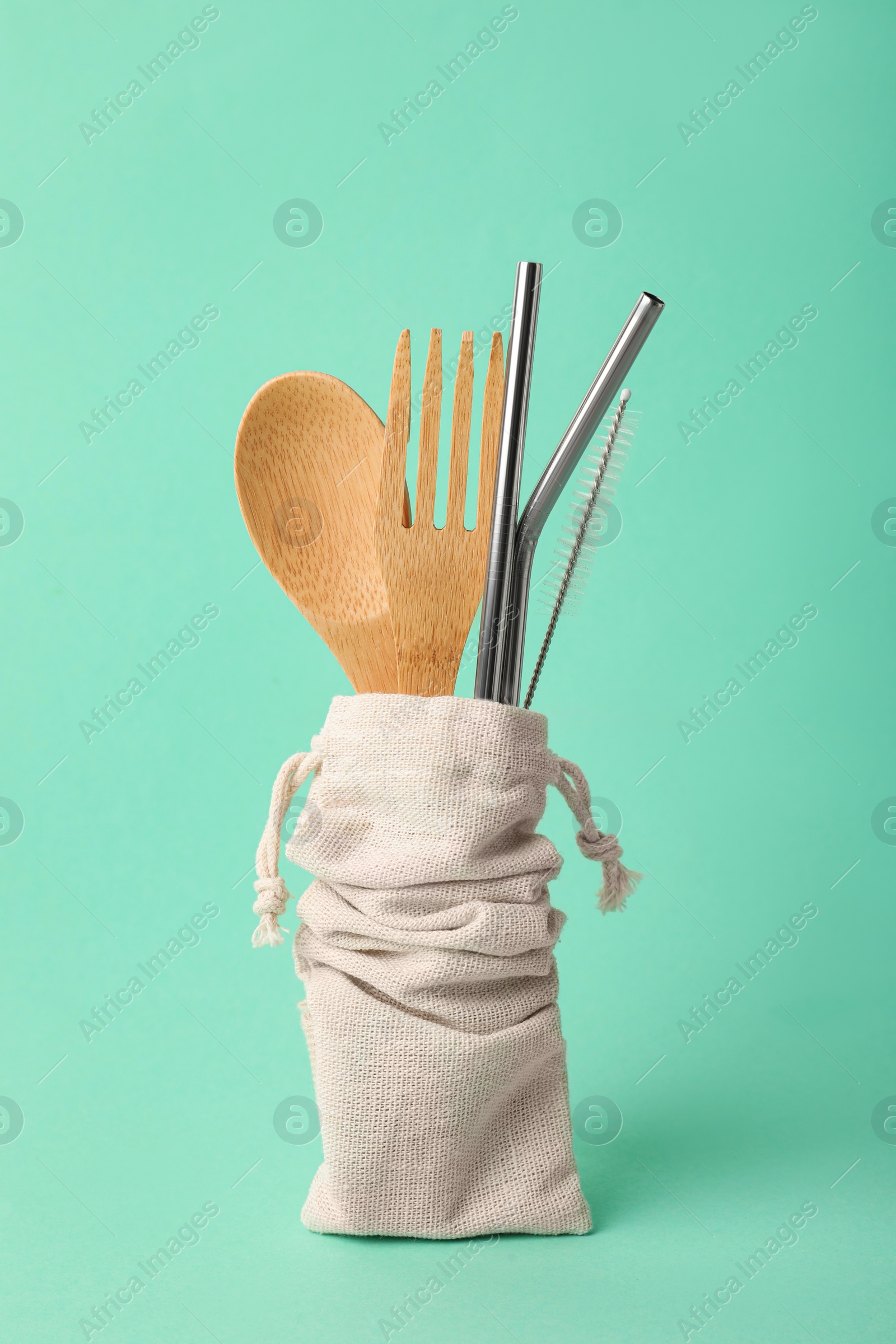 Photo of Bag with bamboo cutlery, metal straws and brush on turquoise background. Conscious consumption