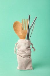 Photo of Bag with bamboo cutlery, metal straws and brush on turquoise background. Conscious consumption