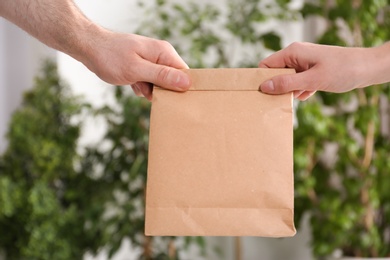 Photo of Man giving blank paper bag to woman on blurred background, closeup. Mock up for design