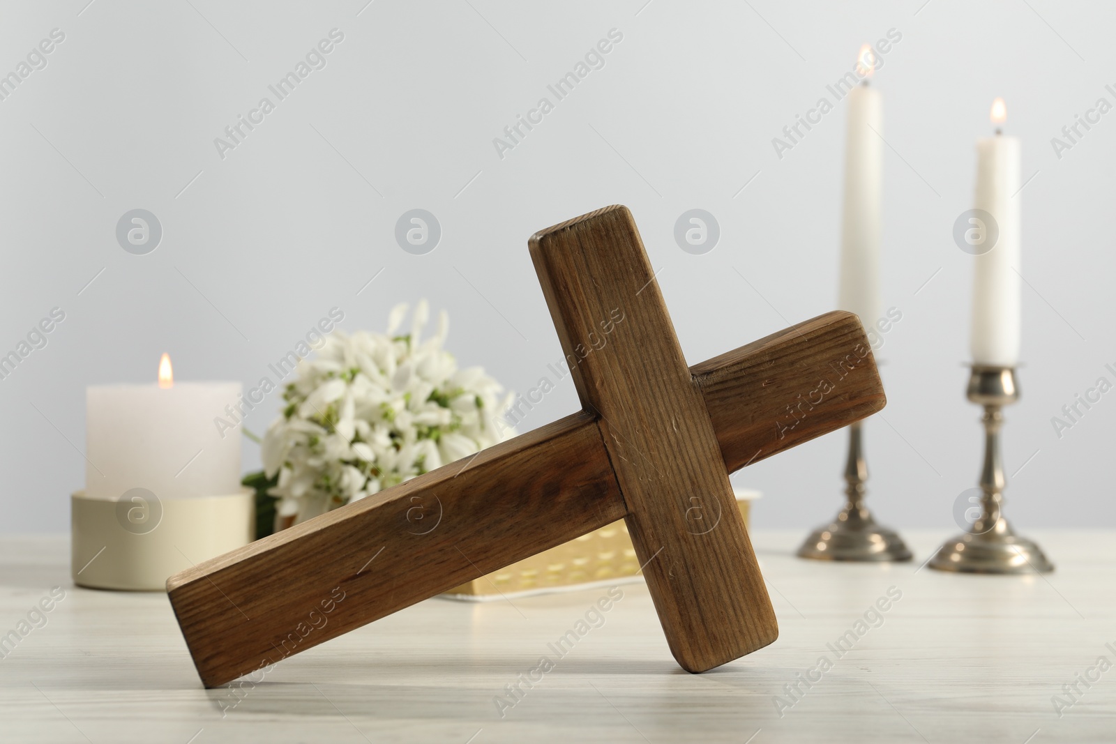 Photo of Burning church candles, wooden cross and flowers on white table