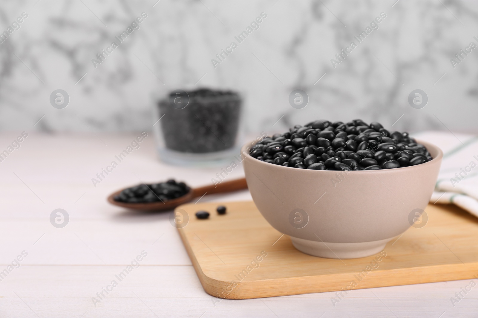 Photo of Bowl of raw black beans on white wooden table. Space for text