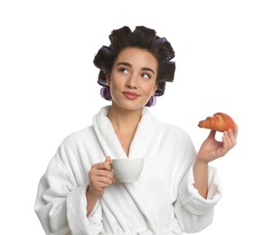 Photo of Happy young woman in bathrobe with hair curlers having breakfast on white background