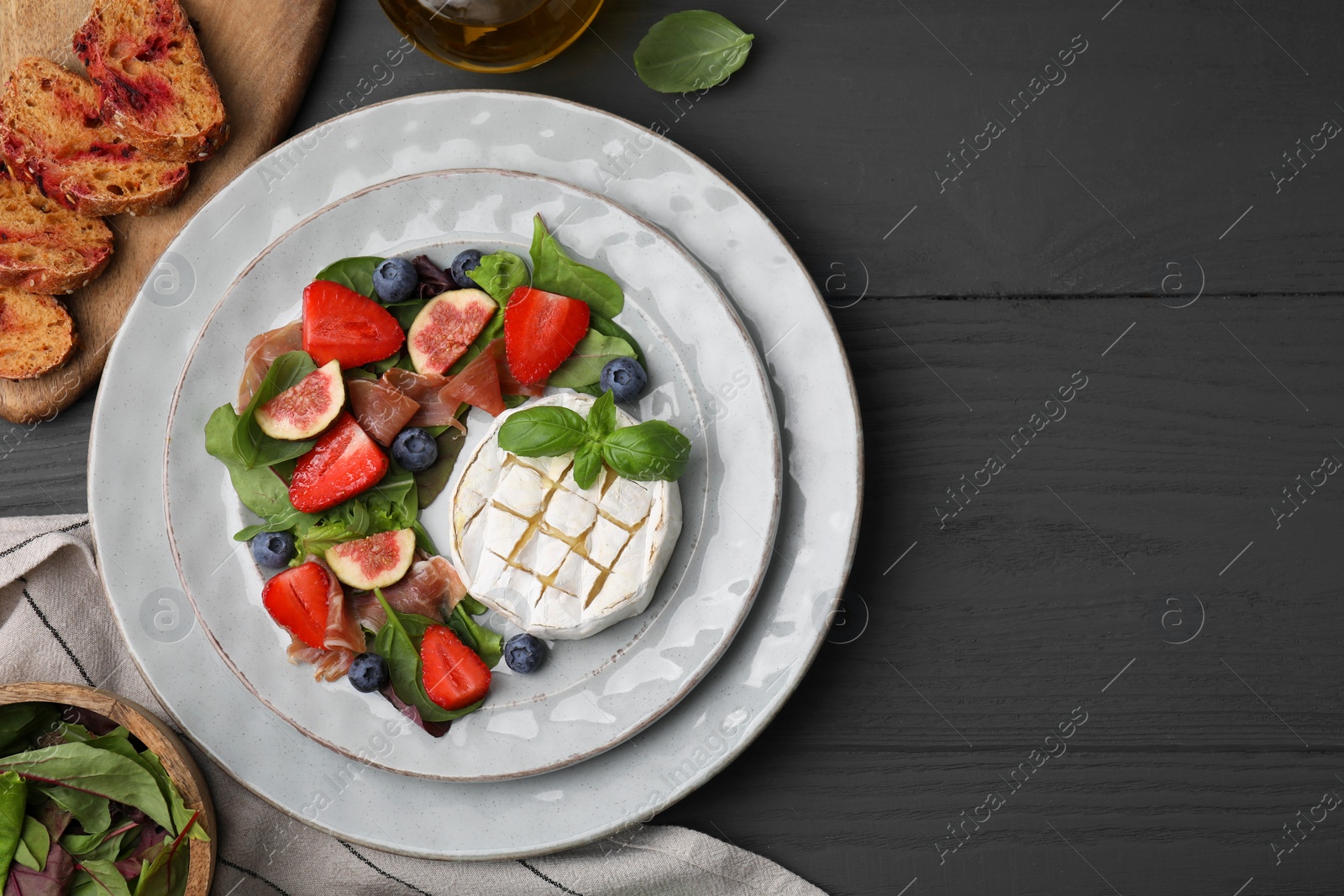 Photo of Delicious salad with brie cheese, prosciutto, figs and strawberries served on grey wooden table, flat lay. Space for text