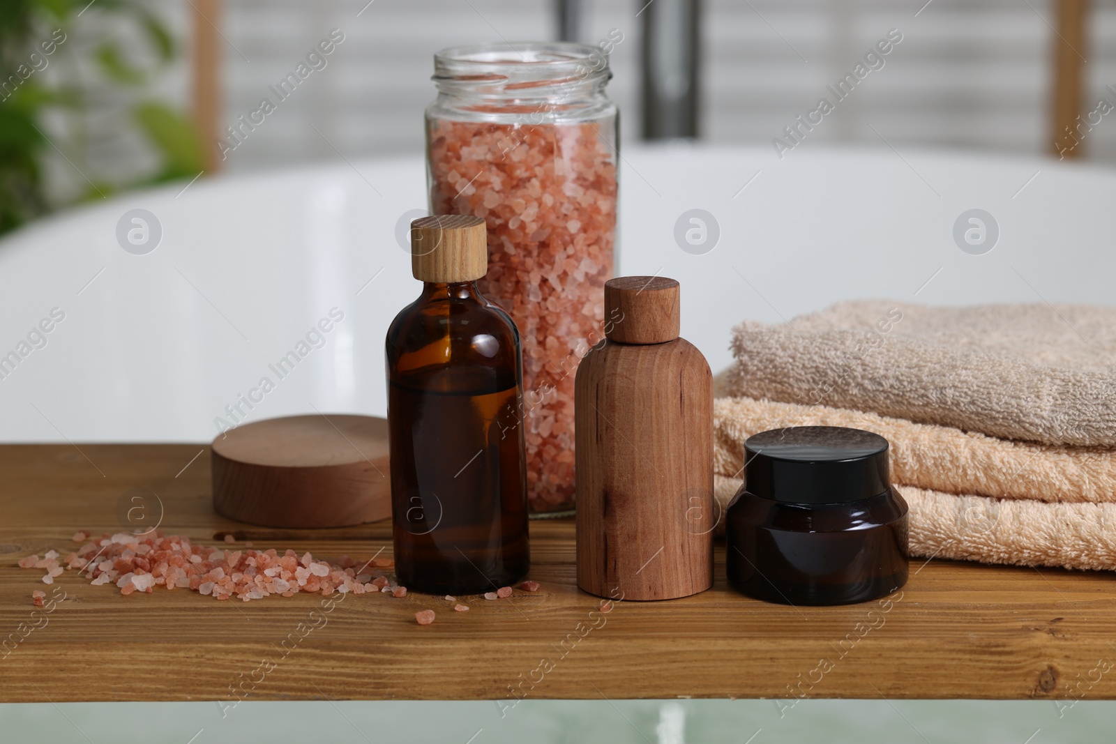 Photo of Wooden board with spa products on bath tub indoors, closeup