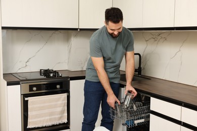 Smiling man loading dishwasher with glasses in kitchen