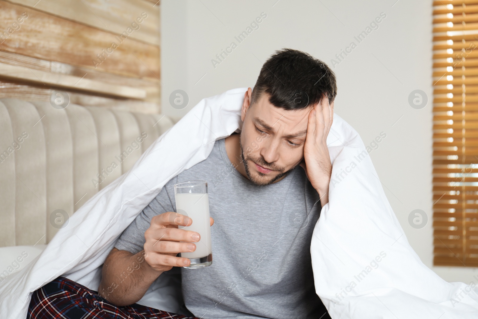 Photo of Man taking medicine for hangover in bedroom at home