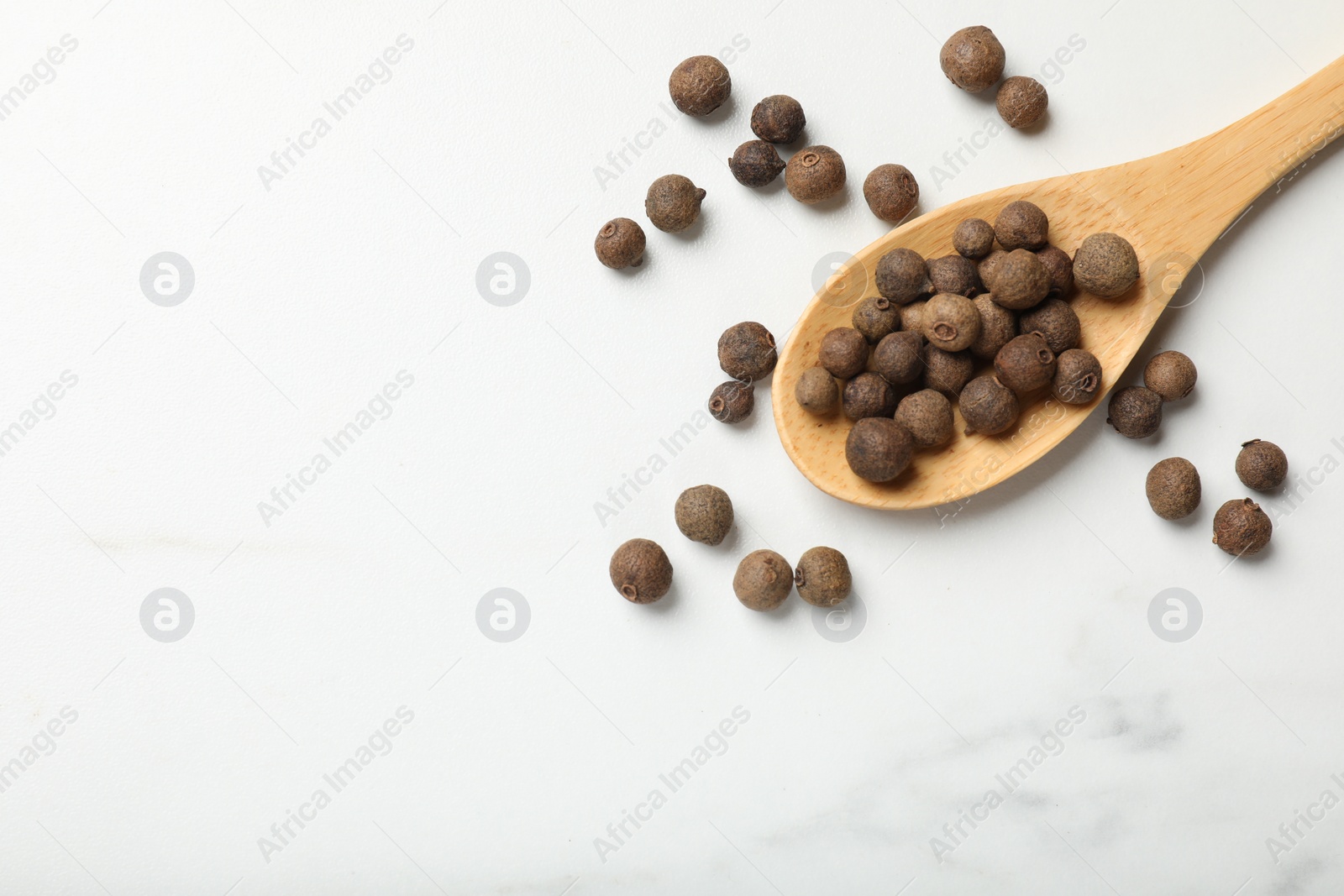 Photo of Dry allspice berries (Jamaica pepper) and spoon on white marble table, top view. Space for text