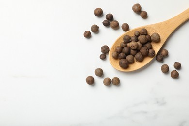 Photo of Dry allspice berries (Jamaica pepper) and spoon on white marble table, top view. Space for text