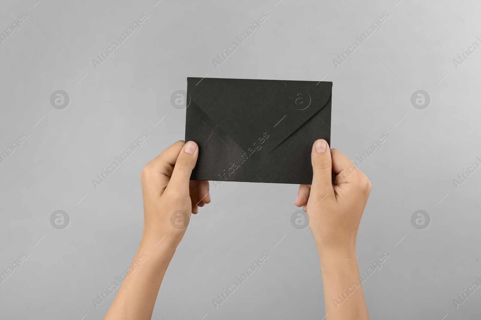 Photo of Woman holding black paper envelope on light grey background, closeup